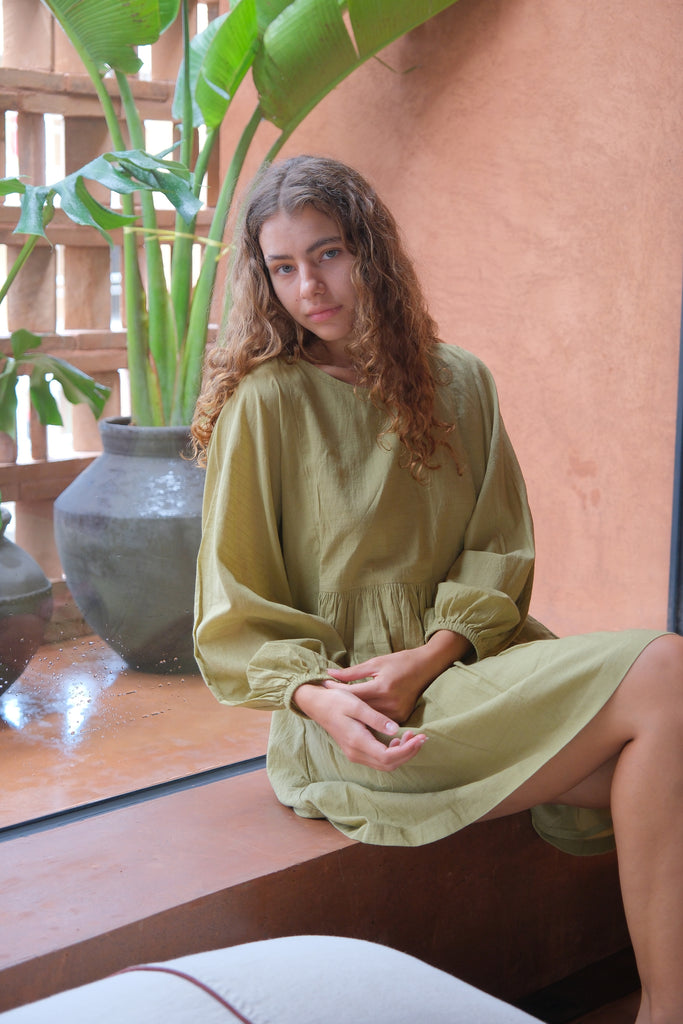 Presenting the Olive Get Away Dress, a collaboration between Audrey E Leary and World of Crow. This unique olive green mini dress features a scoop neckline, three-quarter puff sleeves, and is made from soft, handwoven cotton, offering a breathable, comfortable fit ideal for daily wear.